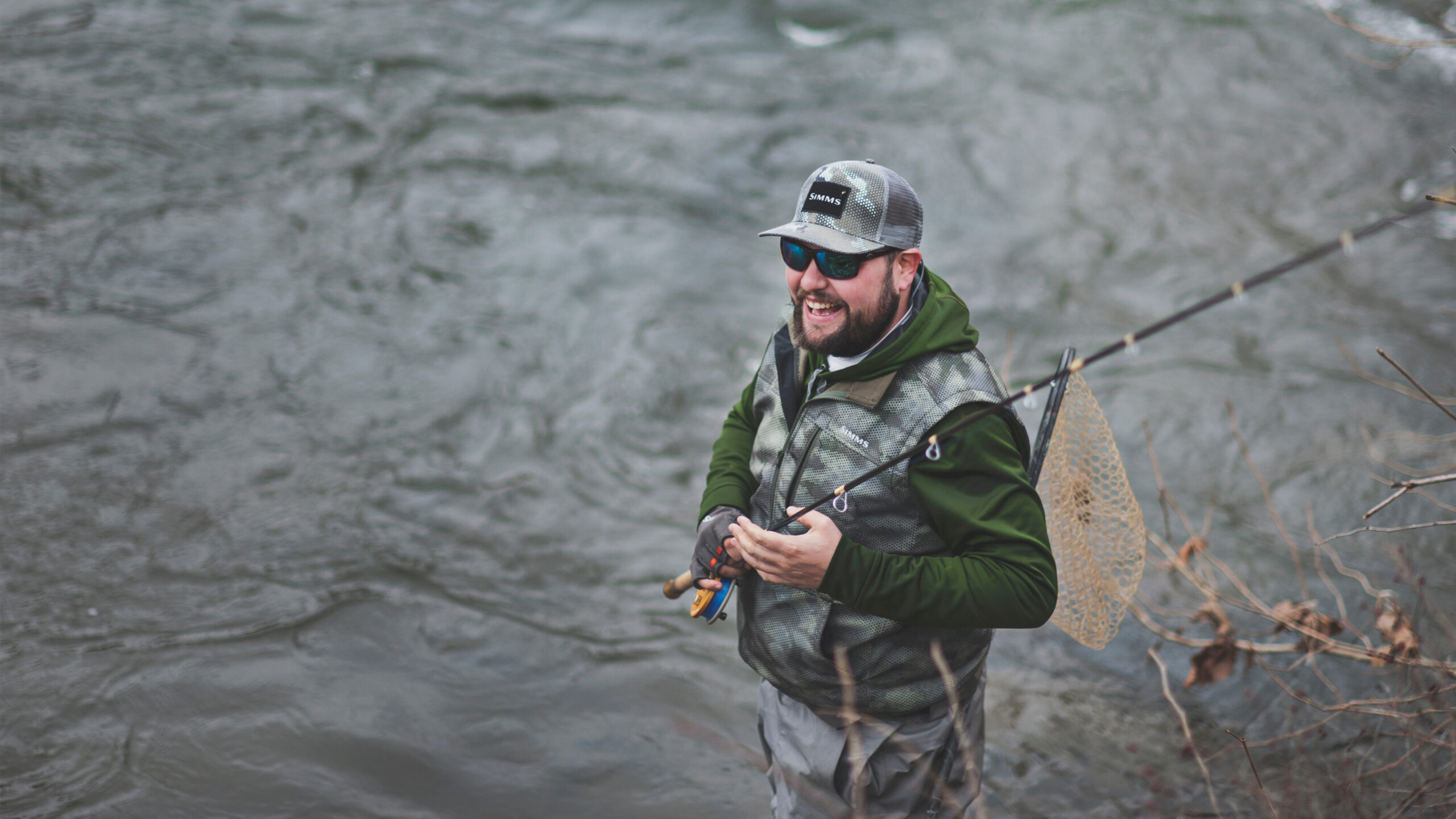 Man in fishing outfit with fishing rod standing in river water