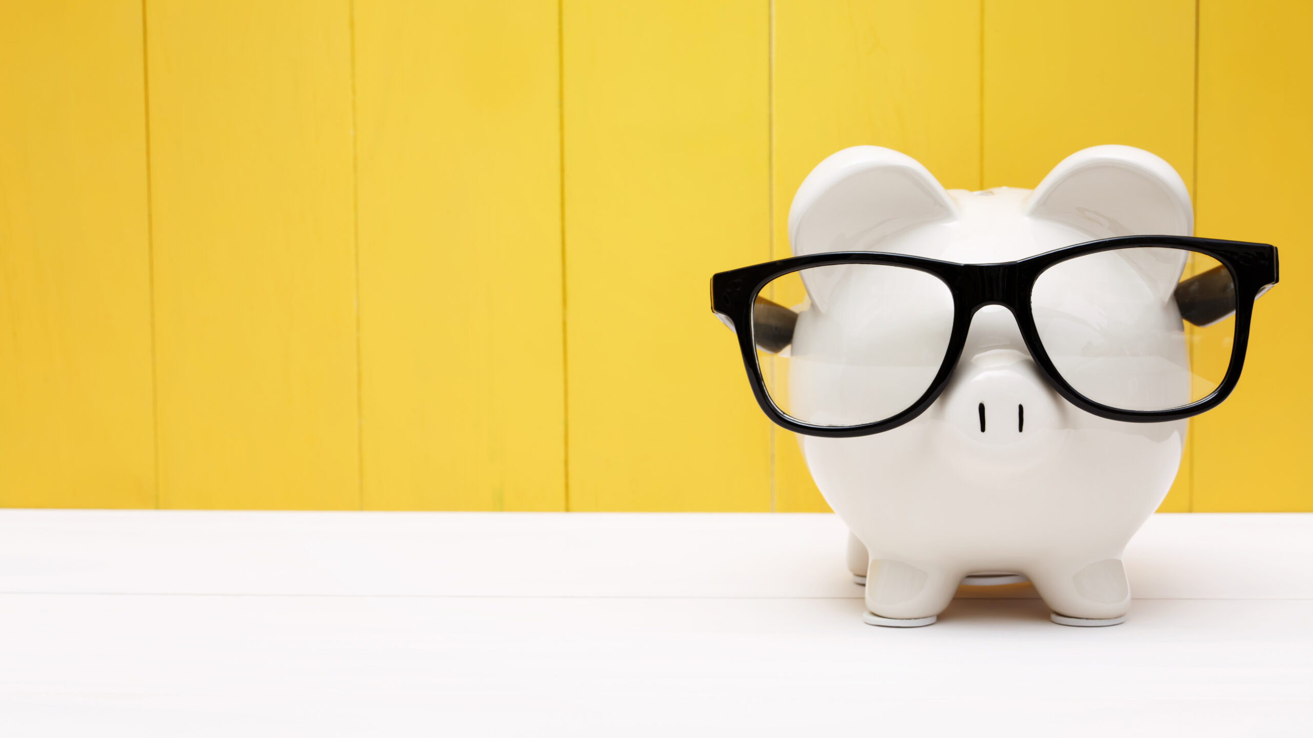 White piggy bank with glasses on against yellow background