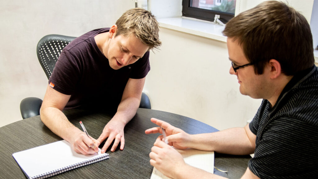 Two people working at a table with notepads and pens