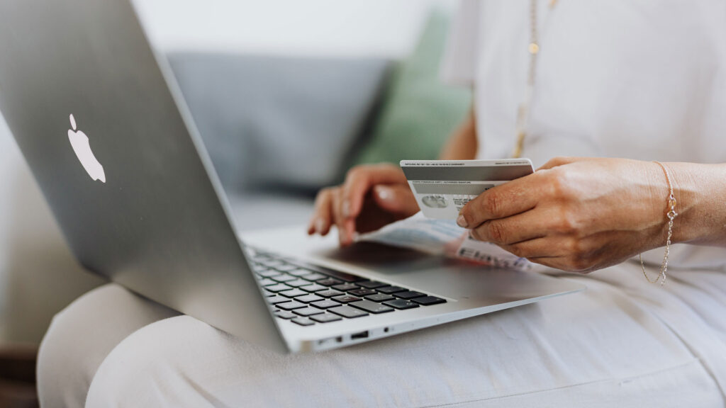 Closeup of person's hand with credit card, in front of laptop example of WooCommerce shopping by BoxUK customised developers