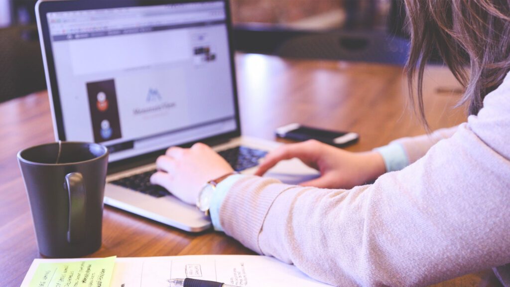 Shot of person using laptop with mug and notes in foreground