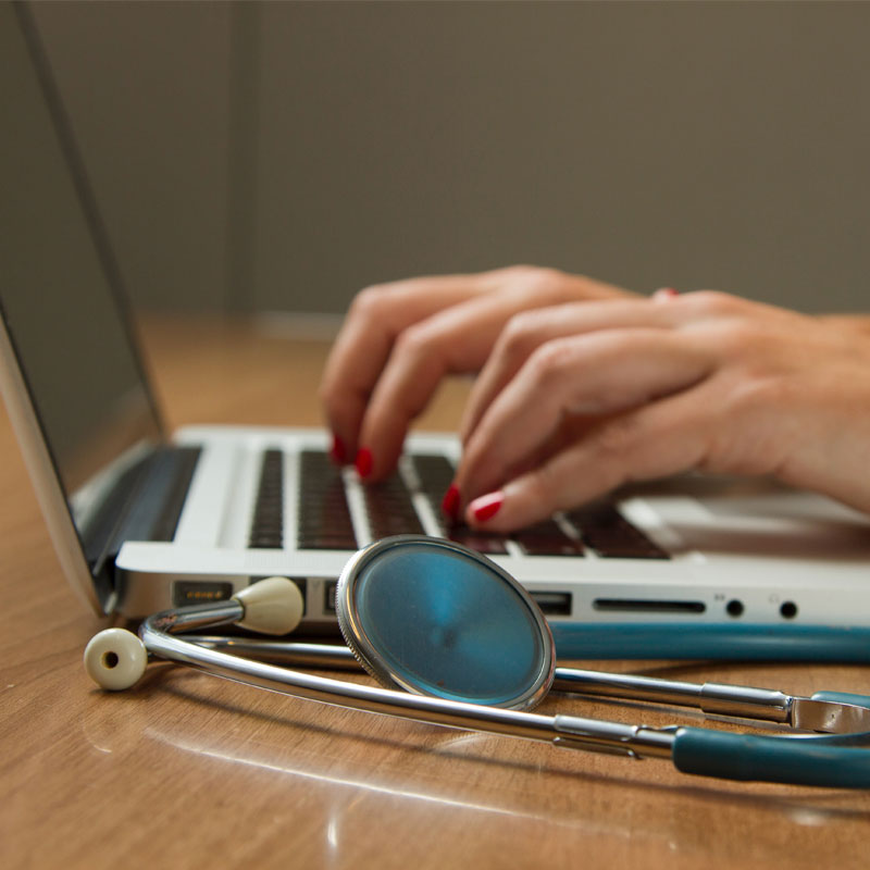 Person working on laptop, with stethoscope in foreground