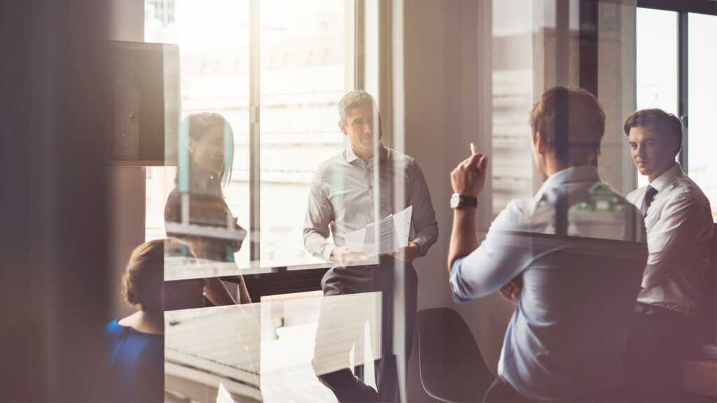 Group of people in a room with glass walls, having a discussion abour using some bespoke software development work from BoxUK