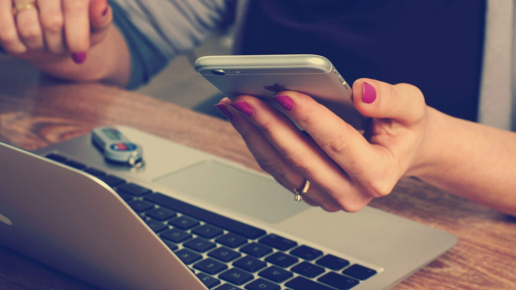 Close up of person holding smartphone and using laptop