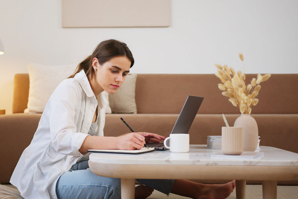 Person sat on floor using laptop and writing pad on low table