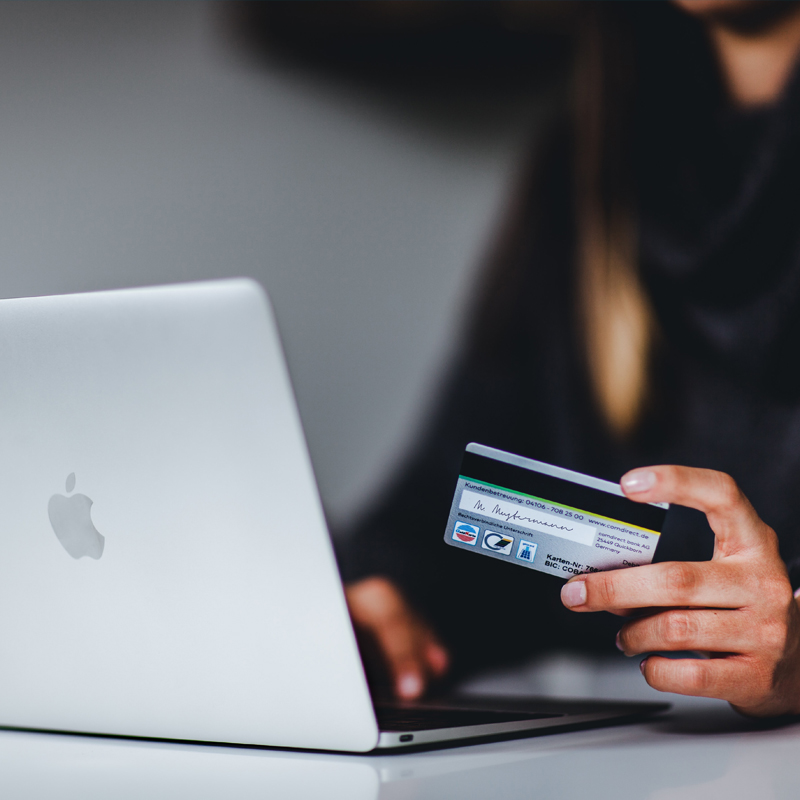 Close up of person holding payment card and using laptop