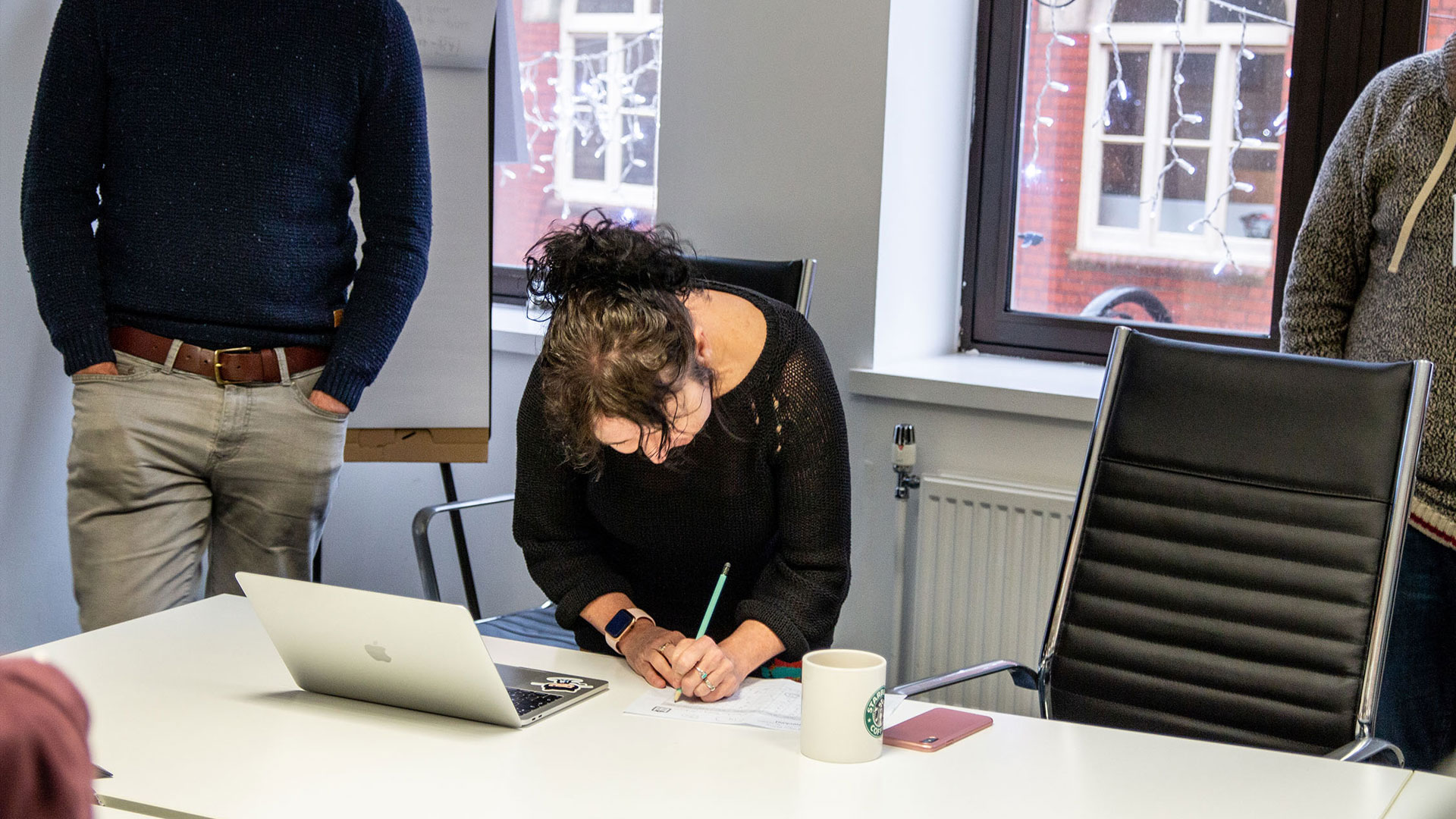 Person writing on a post-it note in front of a laptop