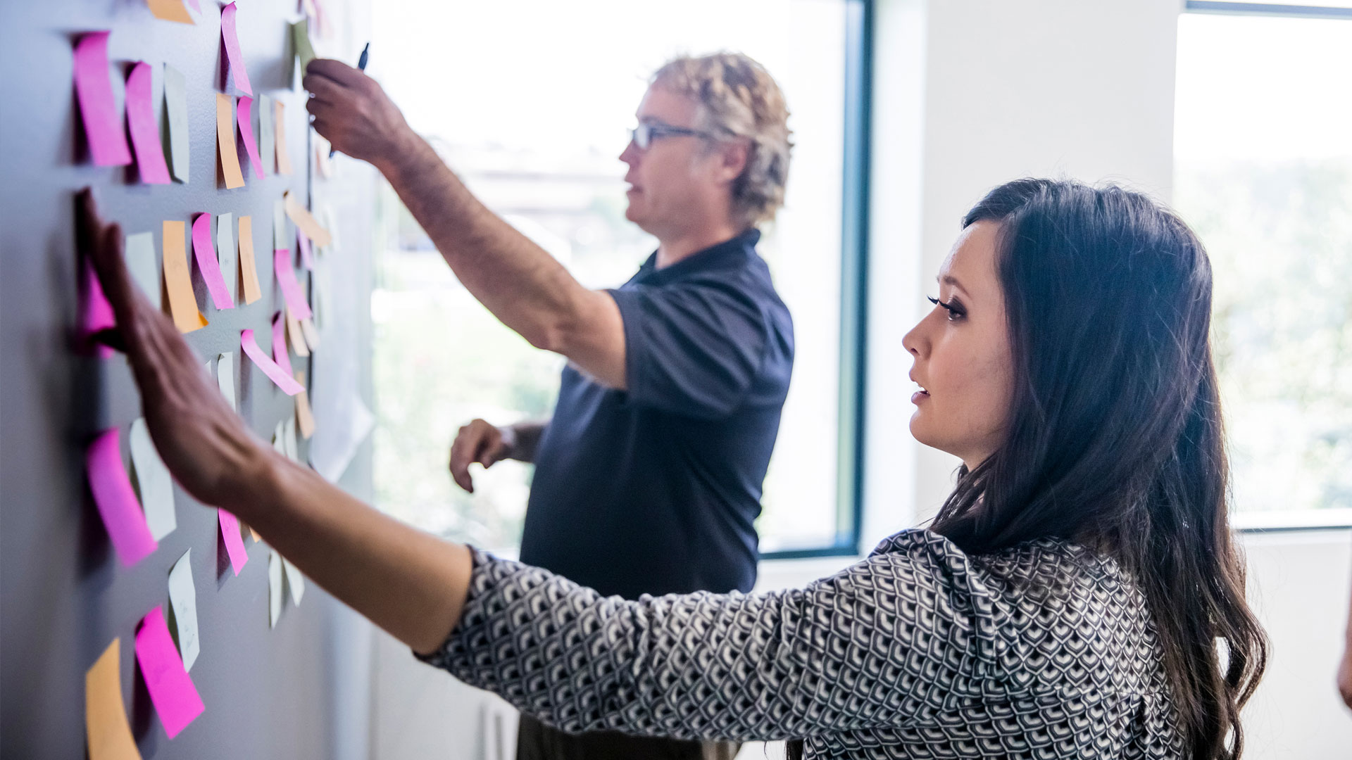 Two people putting post-it notes on a wall